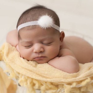 May include: A newborn baby girl sleeping on a yellow blanket with a white headband with a fluffy white pom-pom.
