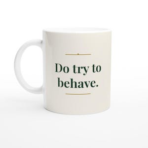 Può includere: Una tazza in ceramica color crema con un carattere serif verde scuro che recita "Do try to behave.". Il testo è centrato tra due sottili linee orizzontali dorate, con un piccolo punto dorato posizionato sopra la linea superiore.