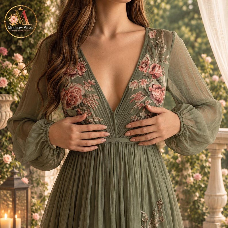 Puede incluir: Un vestido verde salvia de manga larga con un escote en V profundo y un intrincado bordado floral en tonos rosa y crema en el corpi&ntilde;o. La prenda est&aacute; confeccionada en una tela plisada y transparente con pu&ntilde;os fruncidos y falda fluida.