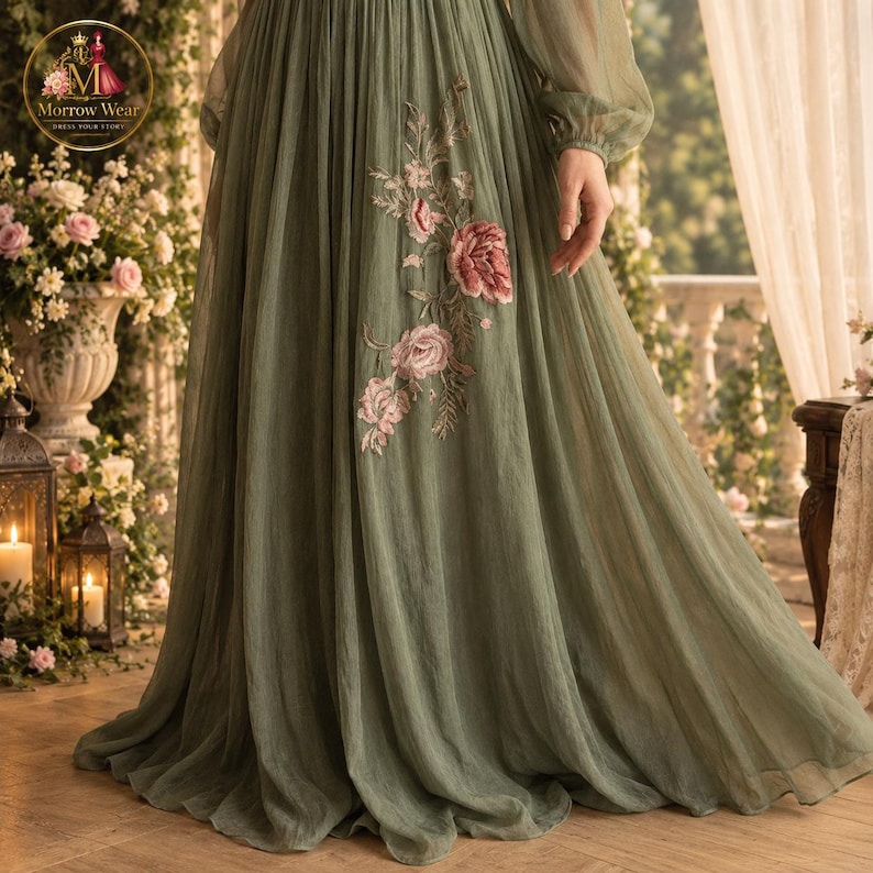 Puede incluir: Un vestido largo de color verde salvia con mangas largas transparentes y falda plisada. La tela est&aacute; adornada con un patr&oacute;n floral bordado en tonos rosa y crema, que cae por el lateral de la falda desde la l&iacute;nea de la cintura.
