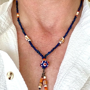 May include: A blue and orange beaded necklace with a large blue and white glass bead pendant. The pendant has a small metal loop and three smaller beads hanging from it.