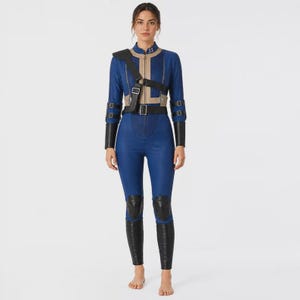 May include: A blue and tan long-sleeved jumpsuit featuring a front zipper, a high collar with the number 33, and a tan vertical panel. It includes black buckled straps across the chest, arms, and waist, along with black knee and forearm guards.
