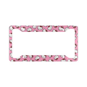 May include: A rectangular license plate frame featuring a repeating pattern of white Hello Kitty character faces with red bows on a solid pink background. The frame has four circular mounting holes, one in each corner, and a wide central opening.