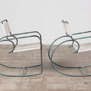Op de afbeelding: Twee vintage schommelstoelen met een lichtblauw metalen frame en witte gevlochten zittingen.