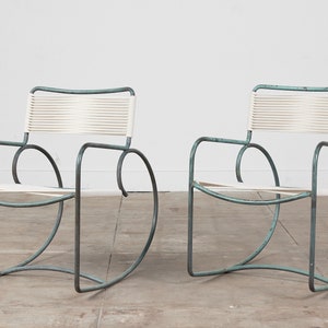 Op de afbeelding: Twee moderne schommelstoelen uit het midden van de eeuw met een witte gevlochten zitting en een poederblauw metalen frame.