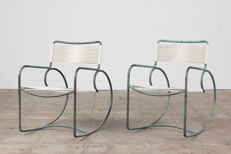 Op de afbeelding: Twee moderne schommelstoelen uit het midden van de eeuw met een witte gevlochten zitting en een poederblauw metalen frame.