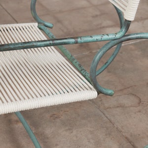Op de afbeelding: Een turquoise metalen schommelstoel met een witte gevlochten zitting.