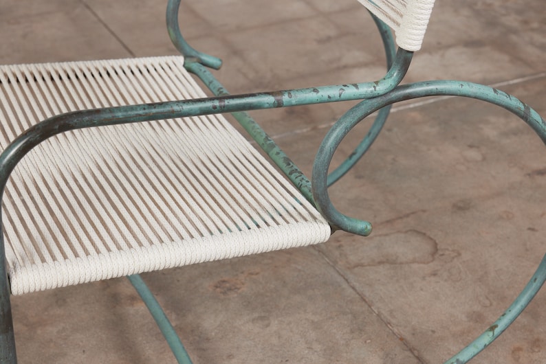 Op de afbeelding: Een turquoise metalen schommelstoel met een witte gevlochten zitting.