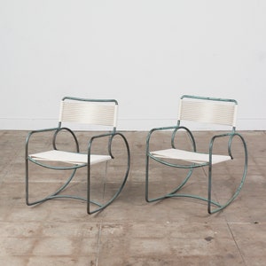 Op de afbeelding: Twee lichtblauwe metalen stoelen met witte gevlochten zittingen. De stoelen hebben een gebogen, wiegende basis.