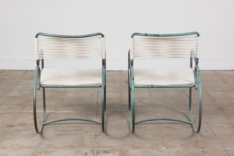 Op de afbeelding: Twee turquoise metalen stoelen met witte touwzittingen. De stoelen hebben een eenvoudig, modern ontwerp en zijn perfect voor buiten dineren of loungen.