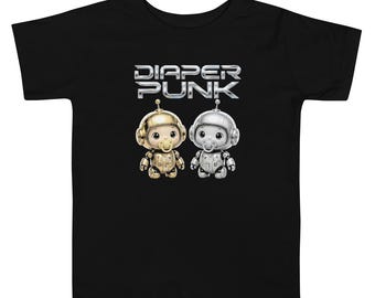 May include: A black short-sleeve t-shirt featuring a graphic of two small robot-like figures, one gold and one silver, each wearing a pacifier. Above the figures, the text DIAPER PUNK is printed in a metallic, stylized font.