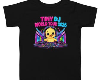 May include: A black t-shirt featuring a graphic of a yellow duckling wearing headphones behind a DJ turntable setup. The text reads TINY DJ WORLD TOUR 2026 in pink and blue letters, accompanied by colorful equalizer bars and star accents.