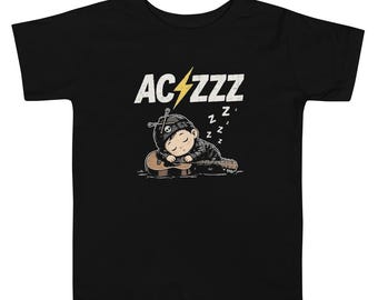 May include: A black t-shirt featuring a graphic of a person wearing a beanie with a skull emblem, sleeping on an acoustic guitar. Above the figure is the text AC/ZZZ with a yellow lightning bolt replacing the slash, and small Zs.