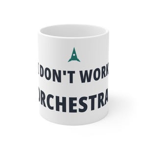 Op de afbeelding: Een witte keramische mok met een donkergroen raketicoon gecentreerd boven de zwarte tekst die luidt I DON'T WORK IN AN ORCHESTRA. De mok heeft een cilindrische vorm met een gladde afwerking en een standaard handvat aan de zijkant van de beker.