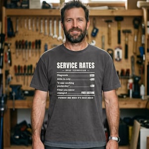 Peut inclure: Un t-shirt gris anthracite à manches courtes avec un texte blanc indiquant SERVICE RATES, HVAC TECHNICIAN, Diagnosis $120, Attic in July +$60, It was working yesterday +$30, Filter you never changed FREE LECTURE, PAYMENT DUE WHEN IT'S COLD AGAIN.