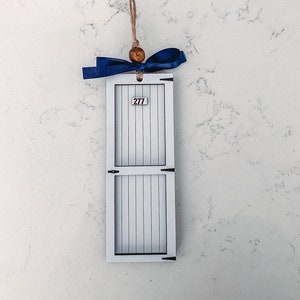 Puede incluir: Una puerta de madera blanca con una cinta azul y una cuenta de madera colgando de una cuerda de yute. La puerta tiene el número "277" en ella.