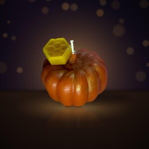 May include: A pumpkin-shaped candle with a metallic orange finish and a white wick. Attached to the top of the candle is a small, yellow, hexagonal honeycomb-shaped wax accent. The candle has a ribbed texture and a rounded, realistic pumpkin form.