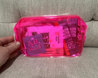 Peut inclure: Une pochette zippée rose néon translucide contenant plusieurs articles, dont une carte carrée violette avec le texte NO SWEAT, un sachet rose vif étiqueté WIPE THAT WISH et deux sachets rectangulaires de mélange pour boisson électrolytique LMNT.