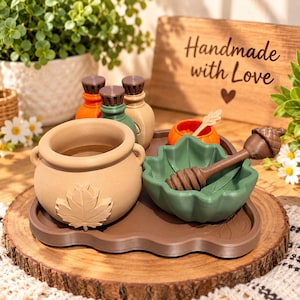 May include: A brown tray holding a beige pot with a maple leaf relief, a green leaf-shaped bowl, a brown acorn-topped honey dipper, and three small bottles with brown caps. The tray features a wooden sign with the text Handmade with Love.