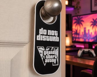 May include: A black and white door hanger featuring the text "do not disturb" and the "Grand Theft Auto V" logo. The rectangular sign has a circular cutout at the top, allowing it to hang securely from a round metal door knob.