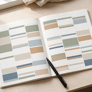 May include: An open planner with white pages featuring a grid layout of rectangular blocks in muted shades of sage green, dusty blue, tan, and cream. The planner contains horizontal lines for writing and a black ballpoint pen rests on the page.