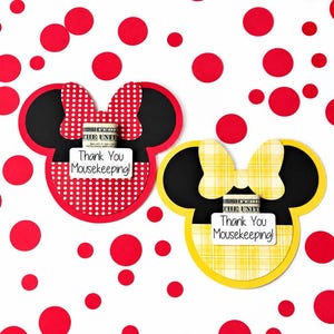 May include: Two paper cutouts shaped like mouse heads with bows. One is red with white polka dots, the other is yellow with a plaid pattern. Each features a rolled dollar bill and a white tag with the text Thank You Mousekeeping!