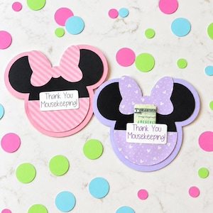 May include: Two paper mouse-shaped cards with black ears and bows. The left card is pink with diagonal stripes and a white label reading Thank You Mousekeeping!. The right card is lavender with a small mouse pattern and a folded dollar bill.