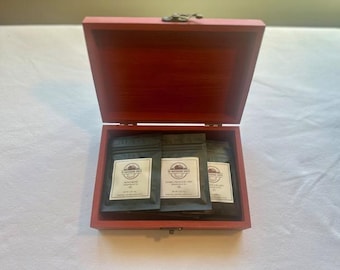 May include: A rectangular wooden box with a red finish and a hinged lid containing three black pouches. Each pouch features a white rectangular label with the text "W. HENDERSON BEE" and "NET WT 2 OZ" printed in black ink, arranged side by side.