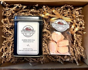 May include: A gift box containing a black rectangular tin of Pumpkin Spice Chai premium black tea and a clear plastic bag of orange pumpkin-shaped candies tied with a gold ribbon. The tin label reads The Underground Grocer, 2 oz / 57 g.