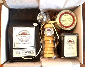 May include: A gift box containing a 12 oz bag of The Underground Grocer coffee, a metal tea infuser, a clear bag of round cookies, a Crumpets & Jam candle in a glass jar, and a tin of The Underground Grocer Earl Grey premium black tea.