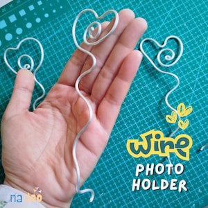 May include: Three silver-coloured metal wire photo holders, each featuring a heart-shaped top with a spiral centre. The text "wire PHOTO HOLDER" is printed in yellow and white on the image, along with small yellow heart icons.