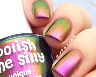 May include: A bottle of Polish Me Silly nail lacquer in a holographic green, pink, and purple color. The bottle is labeled "Polish Me Silly" and "unique nail lacquer" with a 15 ml (0.5 fl. oz.) size.