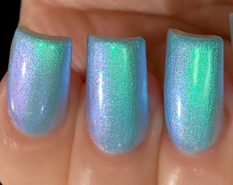May include: Four fingernails painted with a light blue nail polish with a green iridescent shimmer.