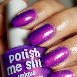 Puede incluir: Una mano muestra u&ntilde;as pintadas de un vibrante color p&uacute;rpura, junto a un frasco de esmalte de u&ntilde;as &uacute;nico "Polish Me Silly". El frasco p&uacute;rpura con texto blanco contiene 15 ml o 0.5 fl. oz. de producto.