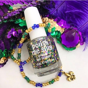 May include: A clear glass bottle of nail polish with gold, green, and purple glitter. The bottle is labeled "Polish Me Silly" and "unique nail lacquer". The bottle is 15 ml or 0.5 fl oz. The bottle is surrounded by a gold and blue beaded necklace with a gold fleur-de-lis charm.