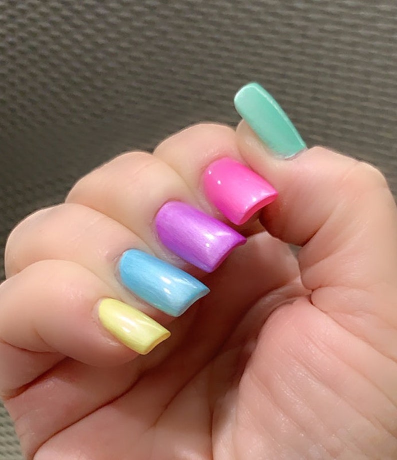 May include: A hand with five fingernails painted in a rainbow gradient. The nails are painted in shades of yellow, light blue, purple, pink, and light green.