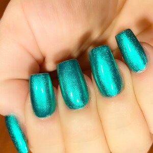 May include: Close-up of five fingernails painted with a bright teal green metallic nail polish.