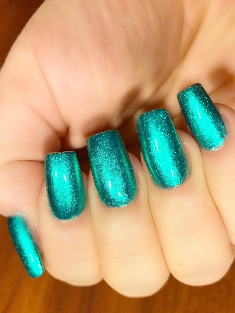 May include: Close-up of five fingernails painted with a bright teal green metallic nail polish.
