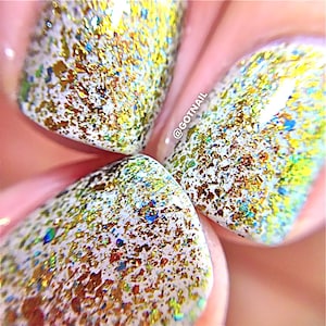 May include: Close-up of manicured nails with a white base and gold, green, and blue glitter flakes. The nails are oval-shaped and have a glossy finish. The text "@GOTNAIL" is visible on the nail.