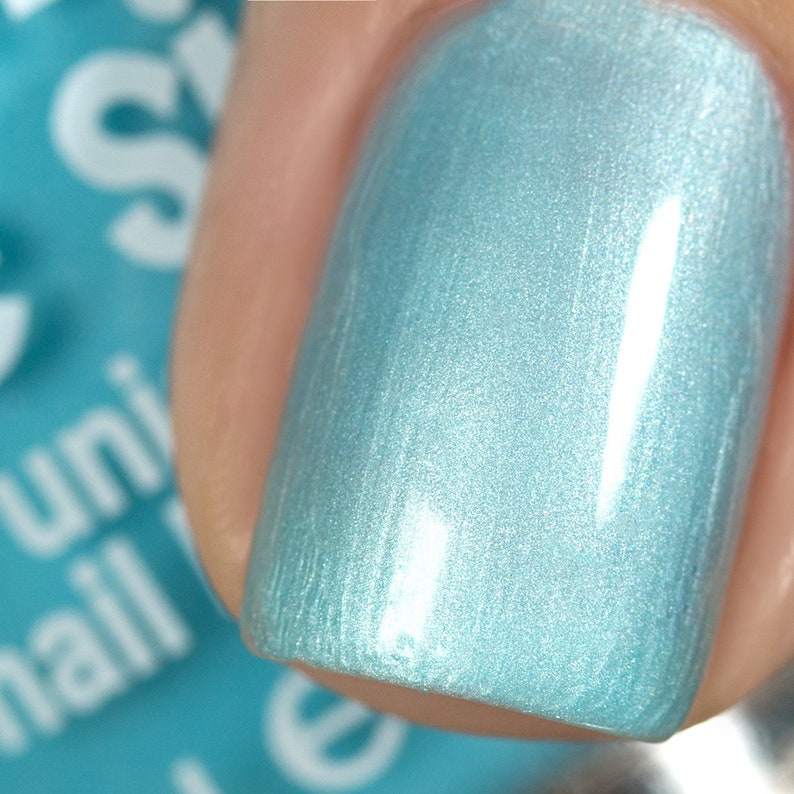 May include: Close-up of a light blue nail polish with a shimmery finish. The polish is applied to a fingernail.