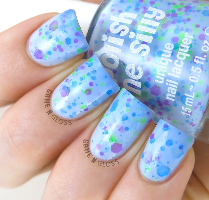 May include: A light blue nail polish with a clear base and multi-colored glitter. The bottle is labeled "Orish ne silly unique nail lacquer 15 mL~0.5 fl. oz".
