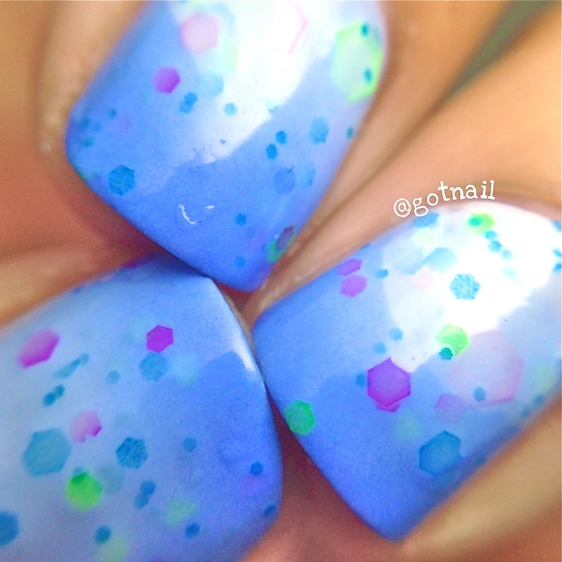 May include: Close-up of three light blue nail polish colors with a variety of colored glitter. The glitter is in different shapes and sizes. The nail polish is on a finger.