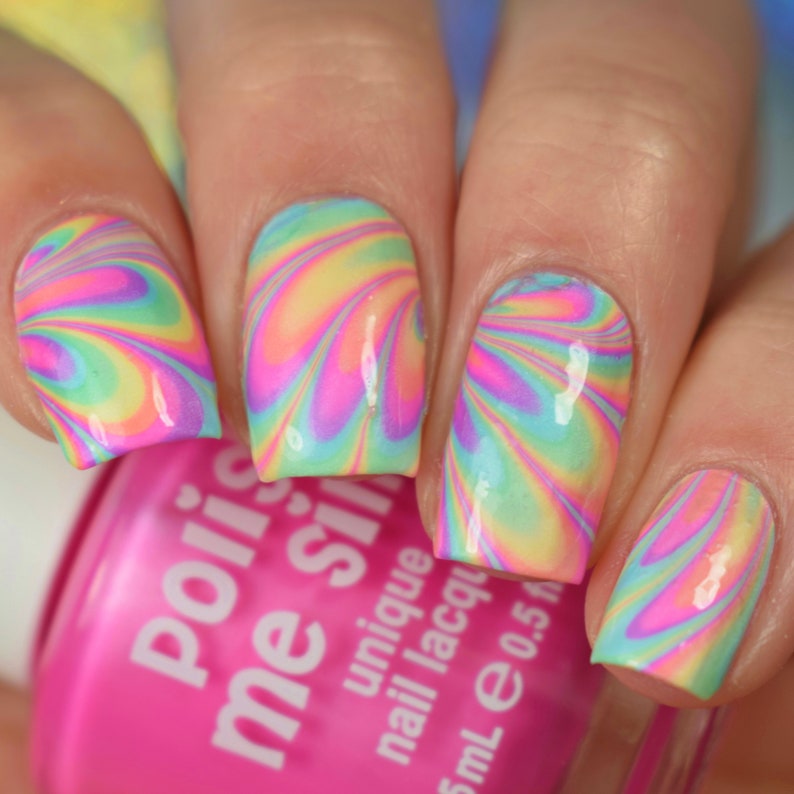 May include: Close-up of a hand with colorful swirl nail art. The nails are painted in a rainbow swirl pattern with pink, yellow, blue, and green colors. The hand is holding a pink bottle of nail polish with the text "Polished" and "Me Silly" on the label.