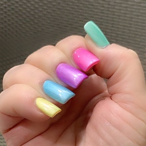 May include: A hand with five fingernails painted in different pastel colors: yellow, light blue, purple, pink, and light green.