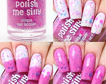 May include: A pink nail polish bottle with a clear label that says "Polish Me Silly" and "unique nail lacquer". The bottle is surrounded by images of fingernails painted with the polish, which has a pink base with white and blue glitter.