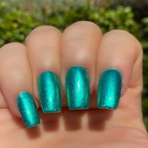 May include: Close-up of five fingernails painted with a teal green nail polish with a shimmer finish.