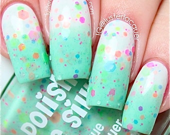 May include: Close-up of fingernails painted with a light green and white ombre nail polish with colorful glitter. The bottle of nail polish is labeled "Polishes" and "The Shine".
