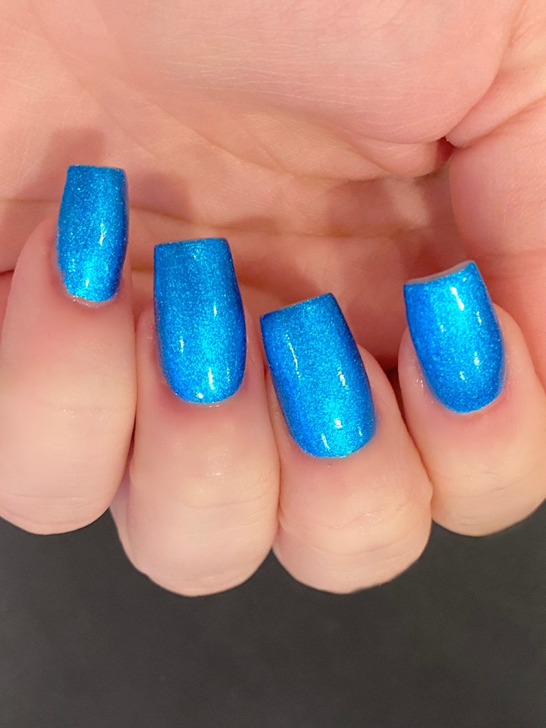 May include: Close-up of four fingernails painted with a bright blue glitter nail polish.