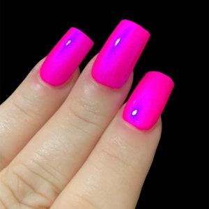 May include: Close-up of three fingernails painted with a bright pink nail polish that has a slight iridescent shimmer.