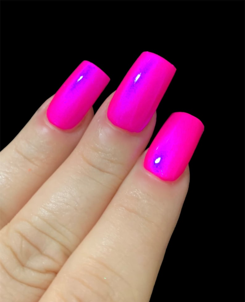 May include: Close-up of three fingernails painted with a bright pink nail polish that has a slight iridescent shimmer.